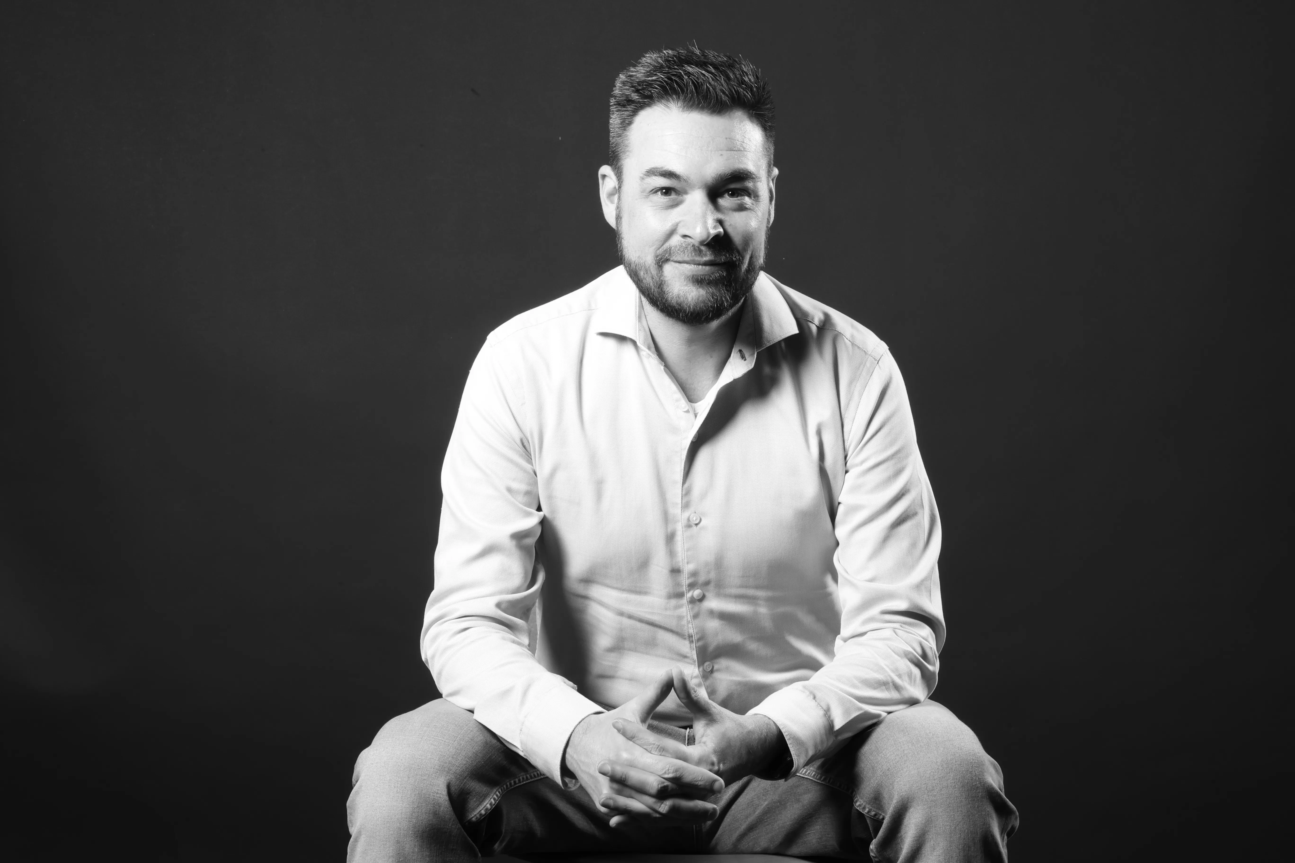 Dennis Poort, zittend, zwart-witportret in een studio-omgeving
